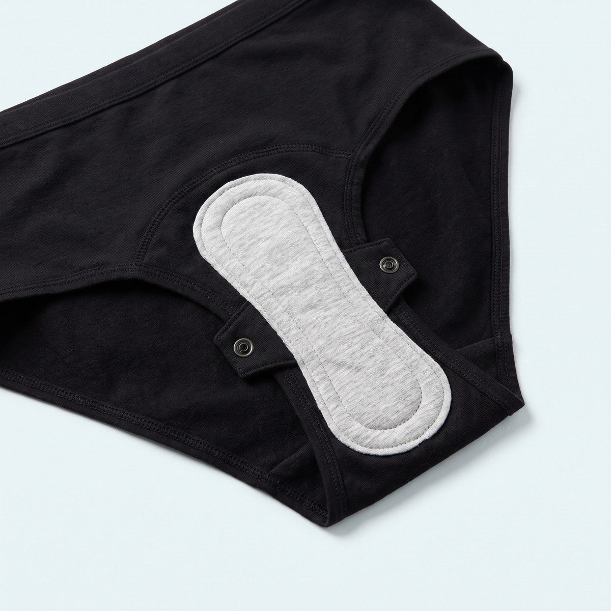 Interno dello slip nero: fondo assorbente e assorbente lavabile agganciato con 2 bottoni a pressione